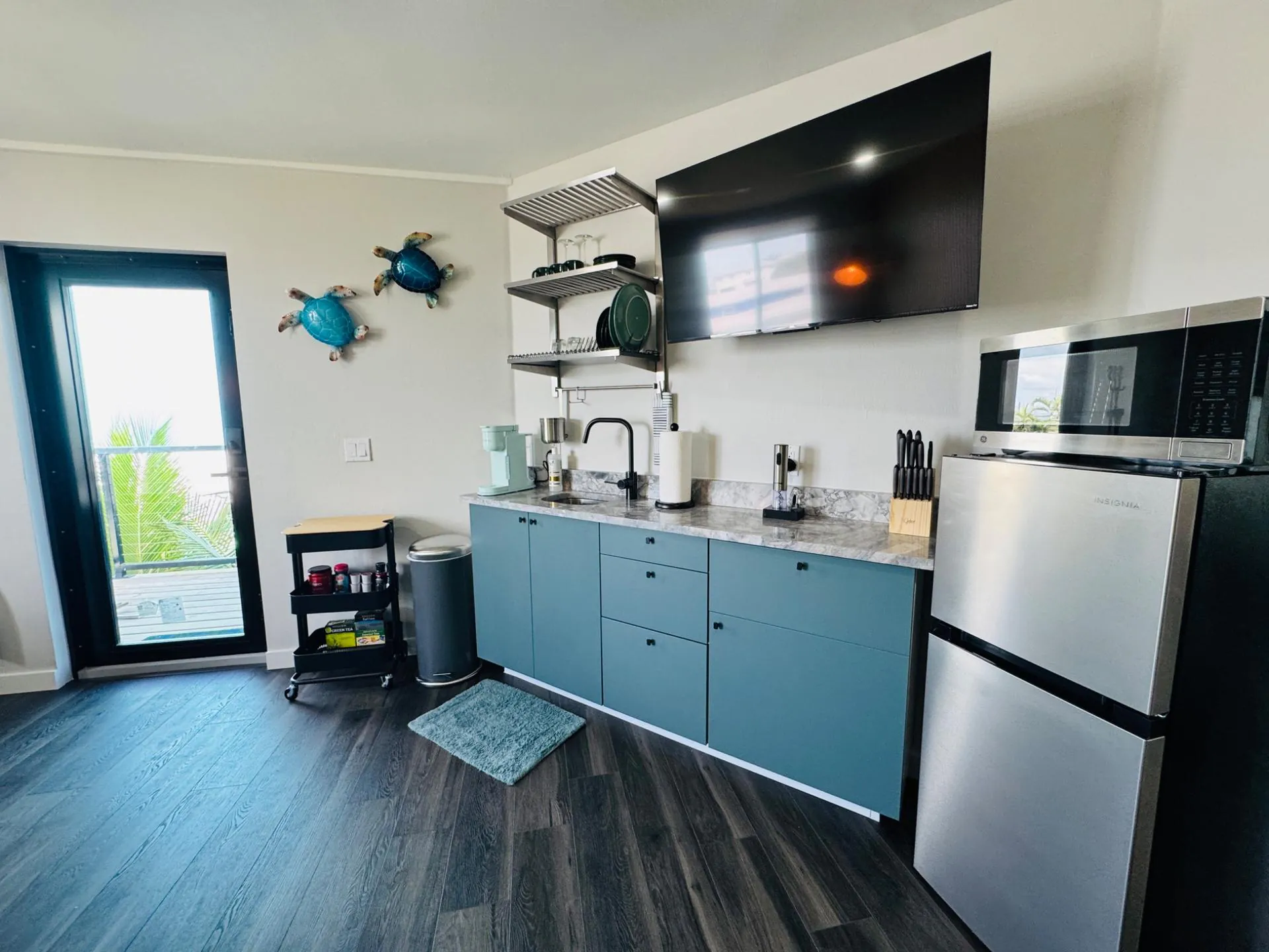 Turtle Suite kitchenette with teal cabinets and a glass door to the deck